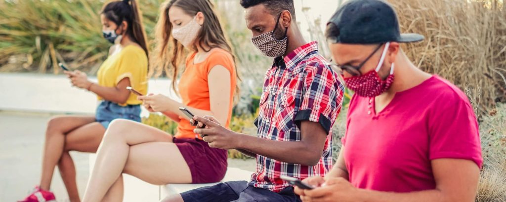 Friends using their smartphones in covid 19 times protected with face mask